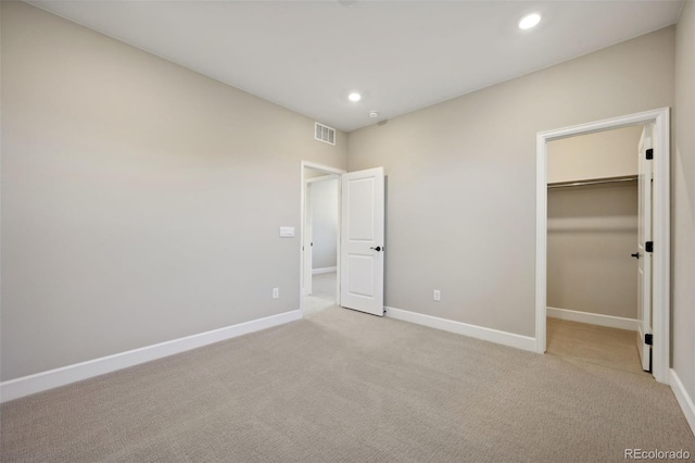 unfurnished bedroom with baseboards, visible vents, light colored carpet, a walk in closet, and recessed lighting