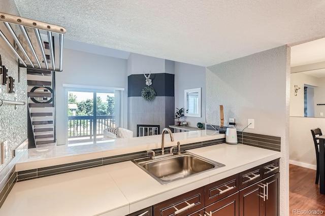 kitchen with a textured ceiling, lofted ceiling, dark brown cabinets, hardwood / wood-style floors, and sink