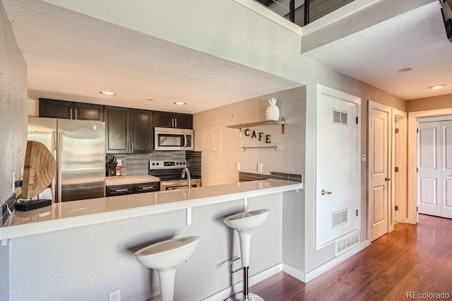 kitchen featuring kitchen peninsula, dark wood-type flooring, stainless steel appliances, a kitchen bar, and decorative backsplash