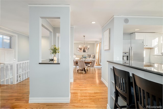 kitchen with white cabinetry, stainless steel refrigerator with ice dispenser, a notable chandelier, ornamental molding, and light hardwood / wood-style flooring