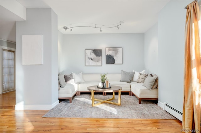 living room with baseboard heating, light hardwood / wood-style floors, and rail lighting