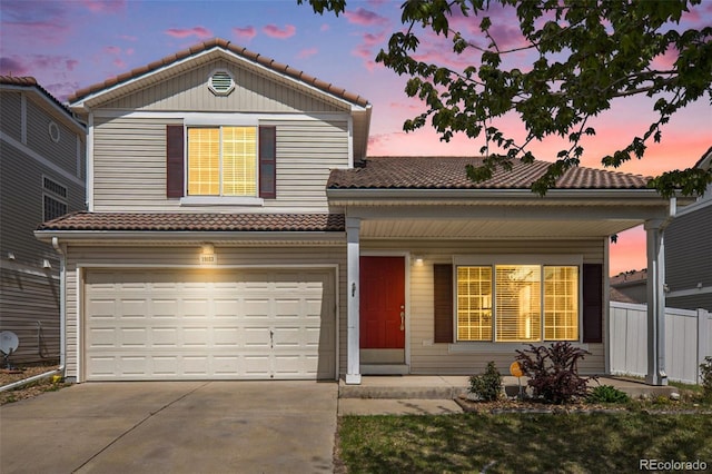 traditional-style home with fence, a tile roof, a garage, concrete driveway, and covered porch