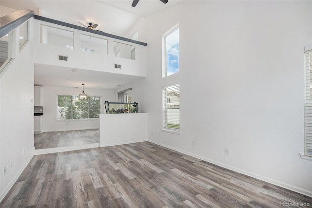unfurnished living room with baseboards, ceiling fan with notable chandelier, wood finished floors, and visible vents
