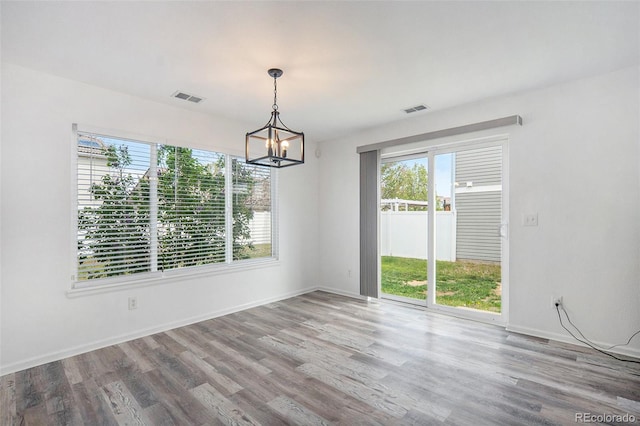 unfurnished dining area with visible vents, baseboards, wood finished floors, and a chandelier