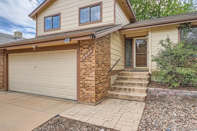 18984 E Kent Cir, Aurora, CO 80013 - view of exterior entry with brick siding, a garage, and a shingled roof