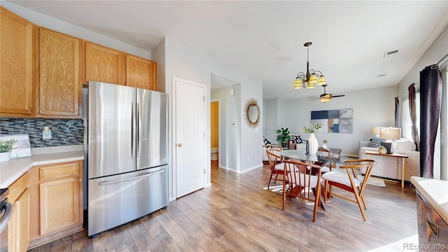 kitchen with ceiling fan with notable chandelier, light countertops, backsplash, freestanding refrigerator, and light wood finished floors