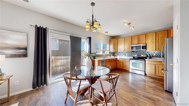 kitchen with a chandelier, wood finished floors, light countertops, appliances with stainless steel finishes, and backsplash