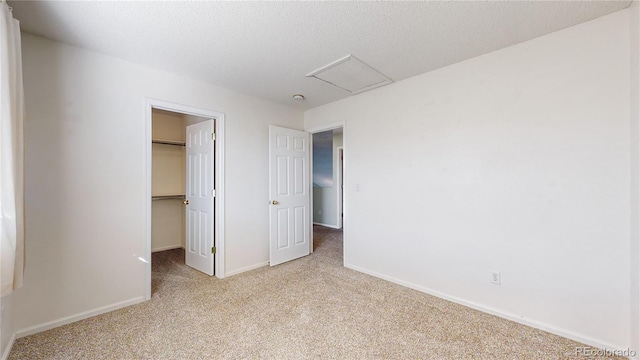 unfurnished bedroom with attic access, baseboards, a walk in closet, a textured ceiling, and carpet floors