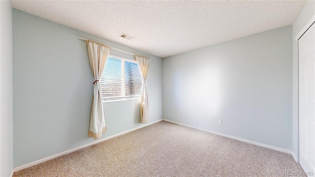 spare room with a textured ceiling, carpet, visible vents, and baseboards