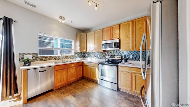 kitchen featuring light countertops, backsplash, light wood-style flooring, appliances with stainless steel finishes, and a sink