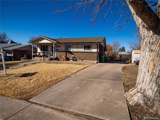 ranch-style house featuring concrete driveway, brick siding, a front lawn, and fence