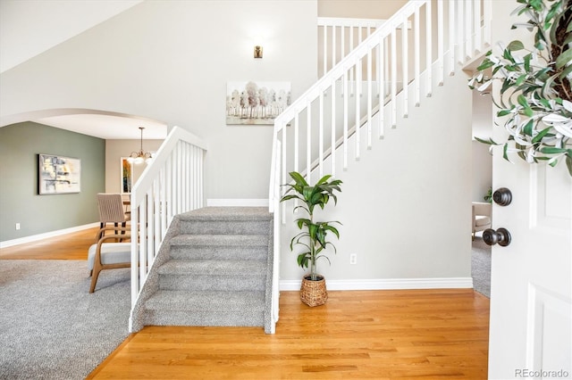 staircase featuring arched walkways, a chandelier, baseboards, wood finished floors, and a towering ceiling