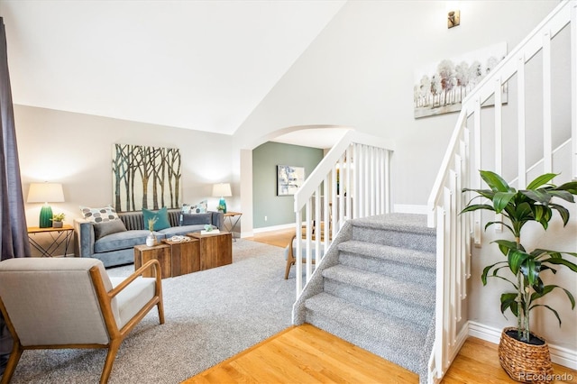 living room with arched walkways, high vaulted ceiling, stairs, baseboards, and wood finished floors