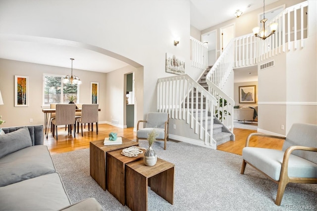 living area featuring visible vents, arched walkways, wood finished floors, a chandelier, and stairs
