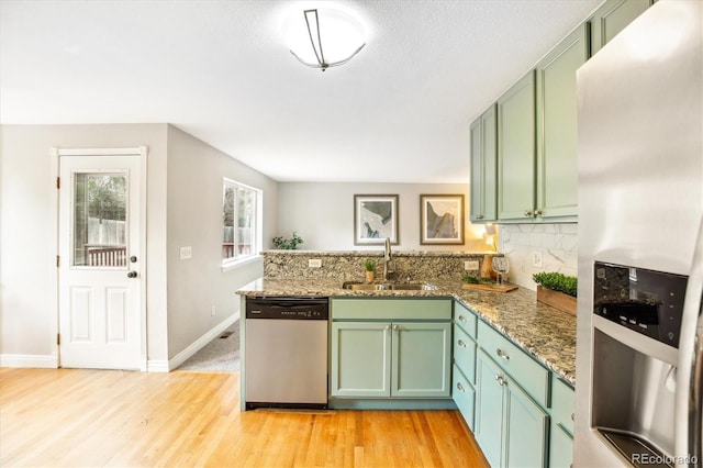 kitchen featuring appliances with stainless steel finishes, a sink, light wood finished floors, a peninsula, and green cabinets