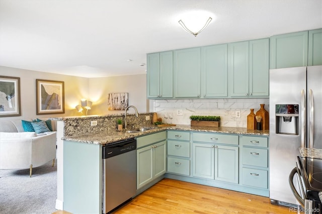 kitchen featuring decorative backsplash, a peninsula, light stone countertops, a sink, and appliances with stainless steel finishes