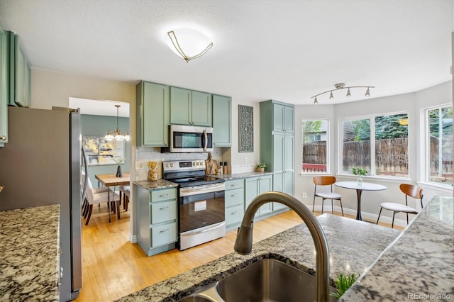 kitchen with a sink, appliances with stainless steel finishes, green cabinets, and light wood-style flooring