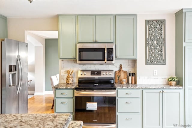 kitchen with backsplash, green cabinets, and stainless steel appliances