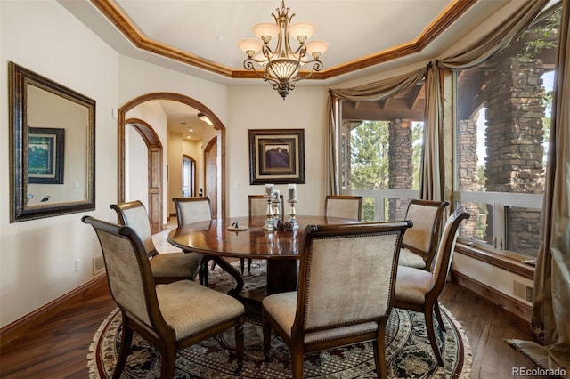 dining area with dark hardwood / wood-style flooring, a tray ceiling, crown molding, and a chandelier