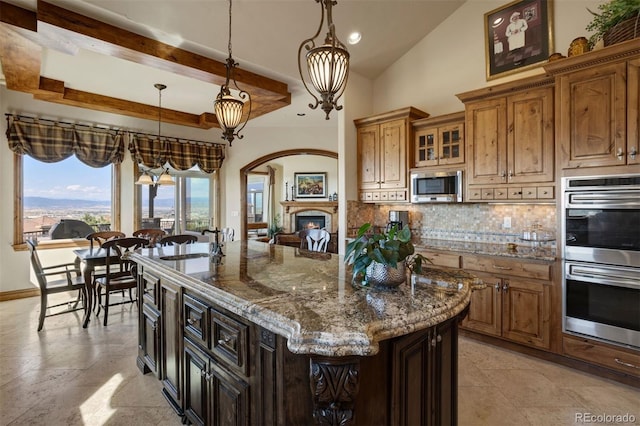 kitchen with backsplash, stainless steel appliances, a kitchen island, decorative light fixtures, and dark stone counters