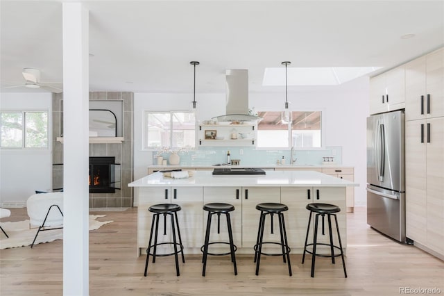 kitchen with island exhaust hood, freestanding refrigerator, a kitchen bar, modern cabinets, and a wealth of natural light