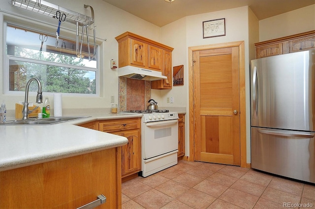 kitchen featuring sink, white gas stove, light tile patterned floors, decorative backsplash, and stainless steel refrigerator