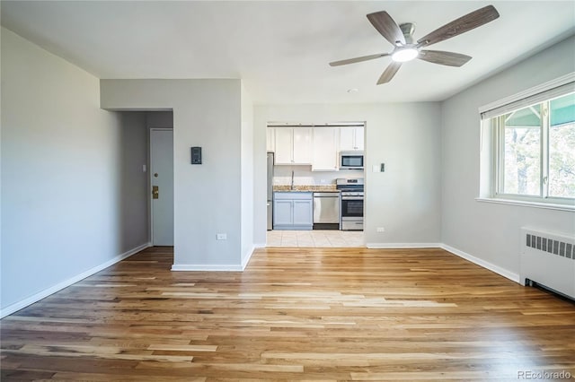 unfurnished living room featuring baseboards, radiator, and light wood-style flooring