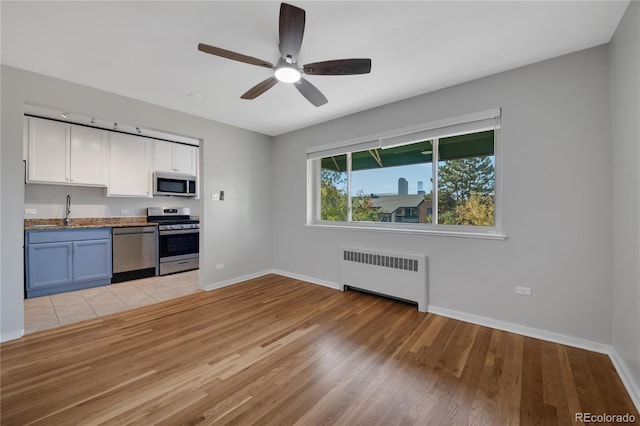 kitchen with light wood finished floors, baseboards, radiator heating unit, appliances with stainless steel finishes, and white cabinetry