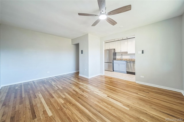 unfurnished living room with a ceiling fan, light wood-type flooring, baseboards, and a sink