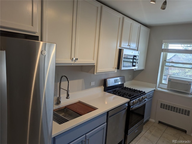 kitchen featuring radiator, light countertops, white cabinets, stainless steel appliances, and a sink