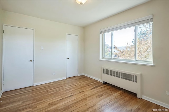 unfurnished bedroom with radiator, baseboards, and light wood-style floors