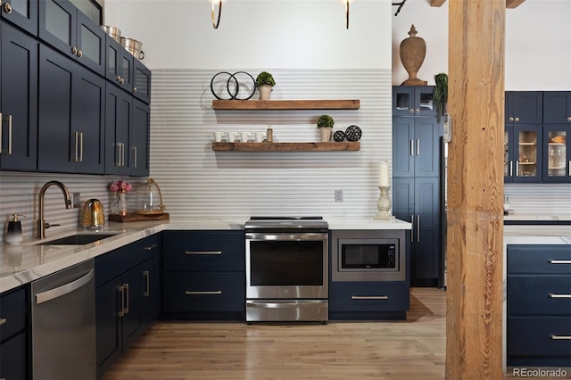 kitchen featuring appliances with stainless steel finishes, decorative backsplash, sink, light hardwood / wood-style floors, and blue cabinets