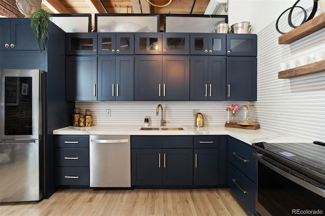 kitchen featuring stainless steel appliances, decorative backsplash, sink, blue cabinetry, and light wood-type flooring