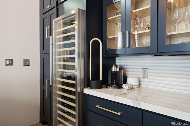 bar featuring blue cabinets, tasteful backsplash, beverage cooler, and light stone countertops