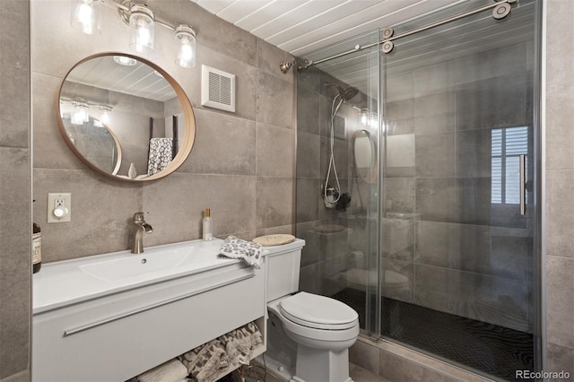 bathroom with toilet, vanity, tile walls, and a shower with shower door