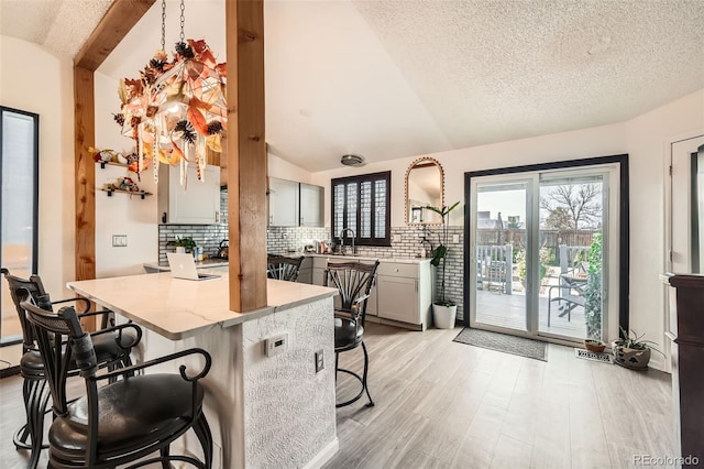 kitchen featuring a kitchen breakfast bar, backsplash, sink, light hardwood / wood-style floors, and lofted ceiling