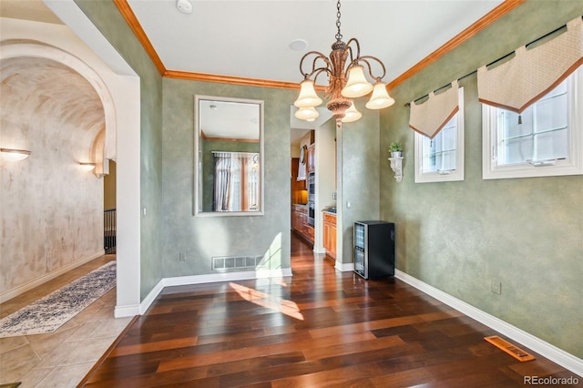 unfurnished dining area with dark wood-style floors, arched walkways, a chandelier, baseboards, and ornamental molding