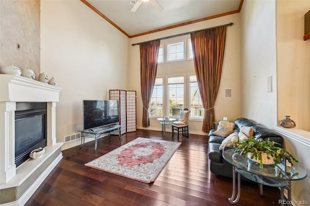 living room featuring ornamental molding, a glass covered fireplace, wood finished floors, ceiling fan, and high vaulted ceiling