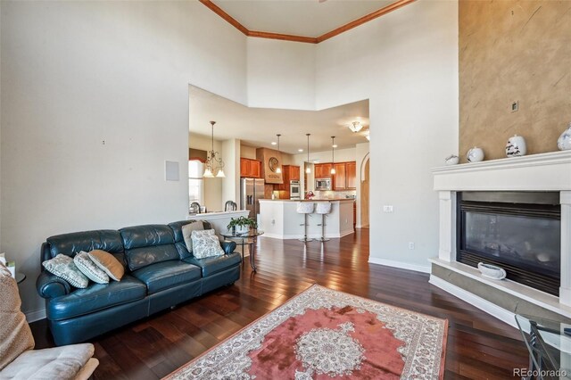 living room with dark wood-type flooring, ornamental molding, a high ceiling, baseboards, and a glass covered fireplace