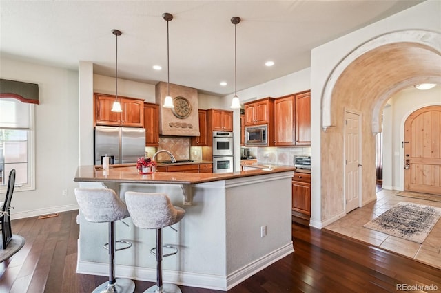 kitchen featuring stainless steel appliances, tasteful backsplash, dark wood finished floors, brown cabinetry, and recessed lighting