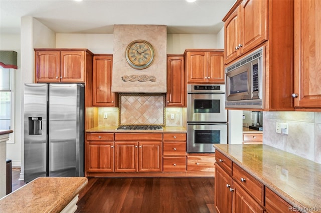 kitchen featuring appliances with stainless steel finishes, dark wood finished floors, light stone countertops, and backsplash