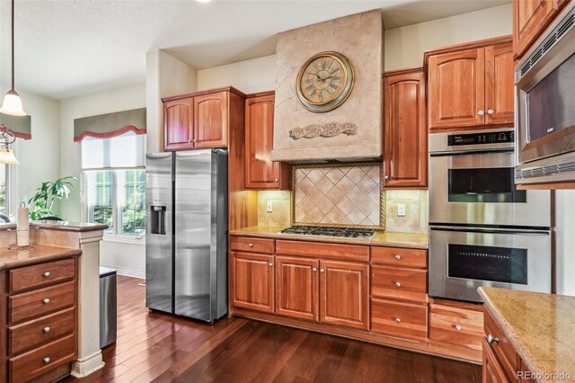 kitchen featuring appliances with stainless steel finishes, dark wood finished floors, exhaust hood, decorative light fixtures, and tasteful backsplash