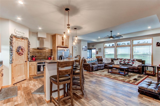 42919 Vista Rdg, Parker, CO 80138 - kitchen with stainless steel appliances, wall chimney range hood, light brown cabinetry, ceiling fan, and light wood finished floors
