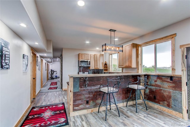 42919 Vista Rdg, Parker, CO 80138 - kitchen with stainless steel microwave, light brown cabinets, light wood-style floors, hanging light fixtures, and a kitchen bar