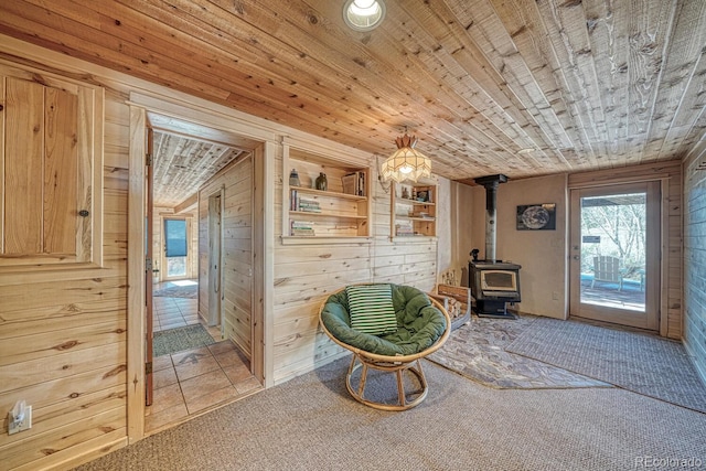 living area with a wood stove, wooden walls, carpet floors, and wooden ceiling