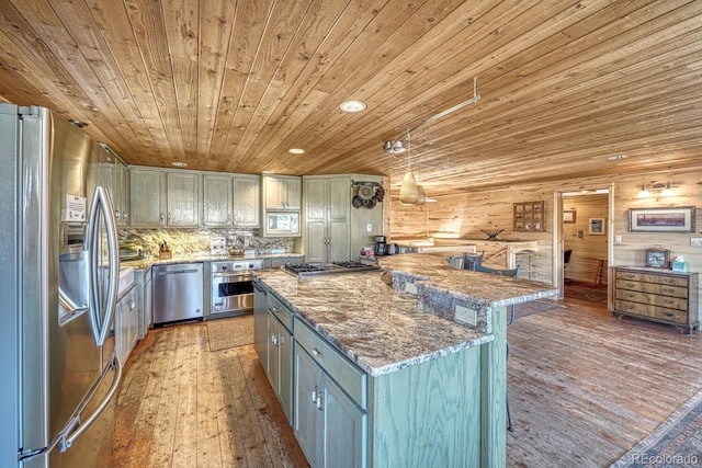 kitchen featuring light wood-type flooring, tasteful backsplash, stainless steel appliances, decorative light fixtures, and wood walls