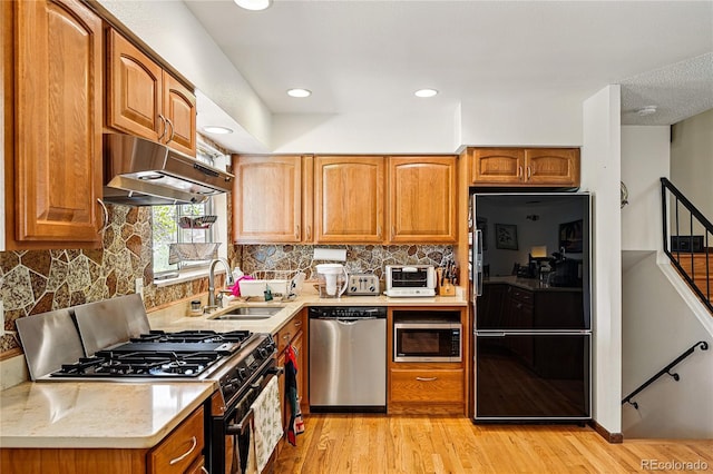7590 E Easter Pl, Centennial, CO 80112 - kitchen with appliances with stainless steel finishes, a sink, under cabinet range hood, light wood-style flooring, and recessed lighting