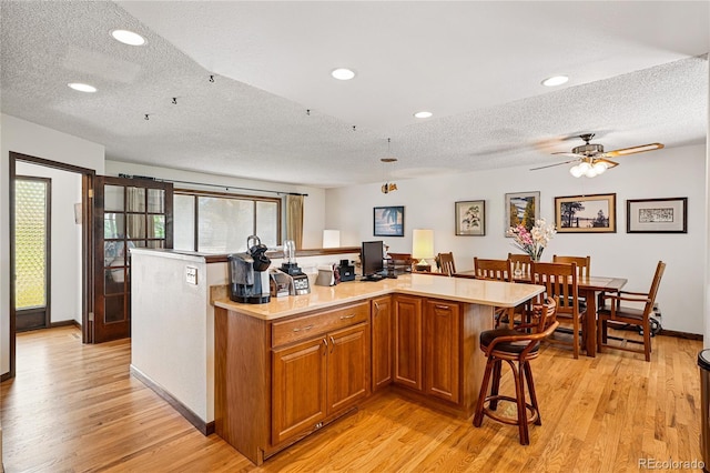 7590 E Easter Pl, Centennial, CO 80112 - kitchen featuring a textured ceiling, light wood-style floors, light countertops, brown cabinetry, and a kitchen bar