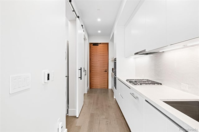 kitchen featuring white cabinets, a barn door, stainless steel gas stovetop, and light countertops