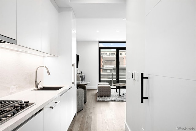 kitchen featuring stainless steel gas stovetop, light countertops, a sink, and white cabinetry